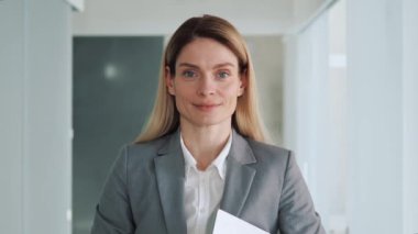 Portrait shot of beautiful Caucasian business woman looking to camera while smiling in office place. Adult entrepreneur, leader, manager posing in hallway. Close up face view business portrait