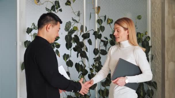中国の投資家とヨーロッパのビジネスオーナーの2人の多様なビジネスパートナーは エコオフィサーの緑の植物を背景に握手し 成功した契約を締結します — ストック動画