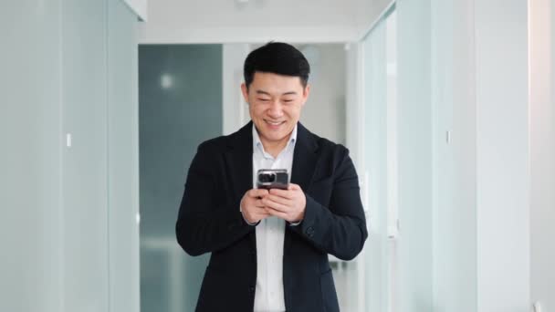 Χαμογελώντας Θετική Ασιατική Επιχειρηματίας Κρατώντας Smartphone Στέκεται Στο Διάδρομο Γραφείο — Αρχείο Βίντεο