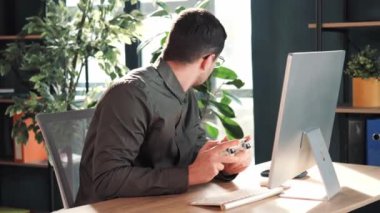 Comic funny office worker happy man employee gamer hold controller joystick playing video game on computer The man looks around to see if anyone is there. Male gamer having fun free time at work