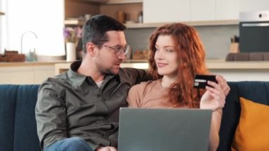 Tarz sahibi mutlu evli çift, dizüstü bilgisayardan satın alan erkek kadın kredi kartıyla ödeme yapıyor evdeki rahat koltukta oturuyor tatmin olmuş yüzler, online alışveriş, satın alma
