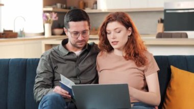 Happy cheerful young couple using laptop holding tickets with passport selecting travel tour plan vacation, choose goods buying clothes on-line on webstore. Shopping together, discuss family rest