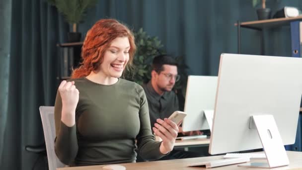 Ενθουσιασμένος Ευτυχισμένος Κόκκινο Μαλλιά Γυναίκα Γραφείο Εργαζόμενος Νικητής Κρατήσει Smartphone — Αρχείο Βίντεο