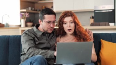Young amazed family happy couple use laptop read news online received great e-mail scream with joy celebrating unbelievable opportunity hugging each other. Lottery win, auction, betting success