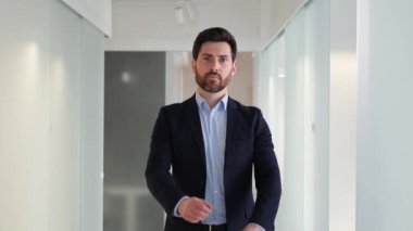 Ofis koridorunda kameraya bakan ciddi ve kendinden emin bir iş adamı portresi. Adam elleri katlı bir şekilde boş bir koridorda duruyor. Sahne profesyonellik, hırs ve başarı barındırıyor..