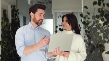 Bitkilerle çevrili yeşil ofisteki dizüstü bilgisayarda işbirliği yapan iki iş arkadaşı fikirlerini tartışıyor. Sağlıklı çalışma ortamı. İşbirlikçi bir şekilde bilgisayar başında, görev işi hakkında canlı bir tartışmaya girişti
