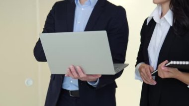 İki meslektaş, erkek ve kadın, yoğun ofis koridorunda yeni bir proje üzerinde birlikte çalışarak, fikirlerini geliştirmek ve işbirliği yapmak için dizüstü bilgisayar kullanıyorlar. Hedeflerine ulaşmak için kararlı bir kararlılık