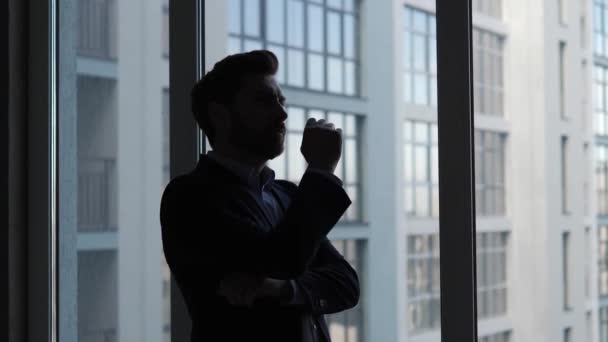 一个商人站在摩天大楼的窗前 陷入沉思 沉思着他在商界的下一个大举动 战略和产生新想法的概念 — 图库视频影像