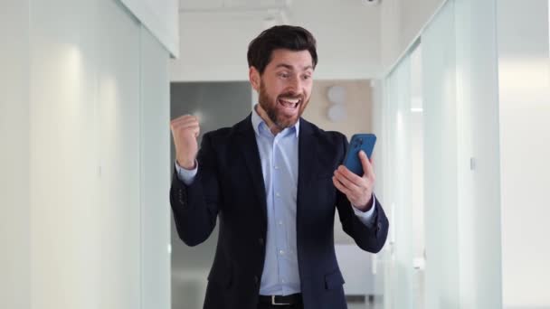 Счастливый Бизнесмен Офисе Смотрит Свой Мобильный Телефон Выигрышной Эмоцией Связанной — стоковое видео