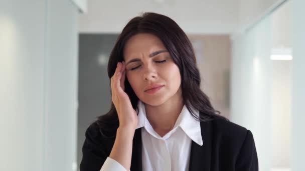 専門的な服装のビジネスマンの女性はオフィスロビーで痛みを伴う頭痛や片頭痛に対処しています おそらく仕事関連のストレスやセルフケアの欠如によって引き起こされます 医療上の注意が必要だ ストレス — ストック動画