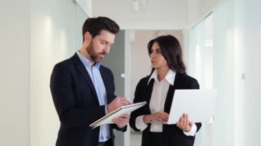 Ofis kadın çalışanları koridorda bir proje hakkında tartışmak ve strateji oluşturmak için dizüstü bilgisayarlar ve kağıt belgeler kullanarak iş birliği yapıyorlar. Teslim tarihlerine ulaşıp hedeflerine ulaşmakta kararlılar.