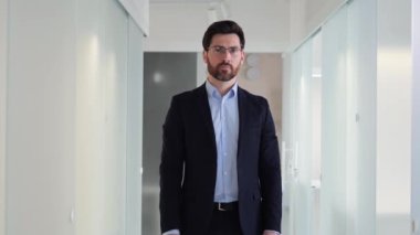 Gülümseyen profesyonel işadamı, bir ofis binasının koridorunda güvenle duruyor ve başarısını ve güvenini yakalıyor. Yakışıklı ve şık giyimli, profesyonellik saçan bir birey.