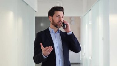 Modern bir ofisin parlak ve çağdaş lobisinde müşterisiyle cep telefonuyla konuşan kendine güvenen bir işadamı. Çoklu görev becerileri ve etkin zaman yönetimi gösteriliyor