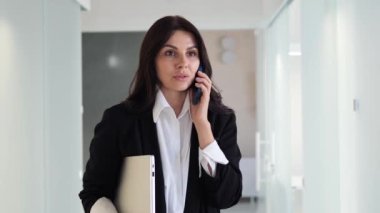 Bir müşterisiyle cep telefonuyla konuşarak şık giyinen ve birden fazla iş yapan meşgul bir iş kadını. Zamanı etkili bir şekilde yönetebilme yeteneği sergileniyor, profesyonelliğini gösteriyor.