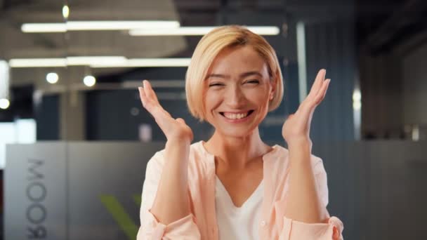 快乐的金发女实业家惊奇地把手放在脸上 在办公室里真诚地微笑着 这预示着一个积极的结果 好消息 获奖者赢得了欢欣 行动的号角 — 图库视频影像