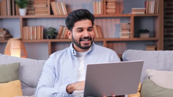 幸せなインド人は彼の家のオフィスでビデオ会議のためのラップトップを使用しています ラップトップの前に座っている男は ビデオ会話に従事しているように見えます 快適な個人的なリモート会話 — ストック動画