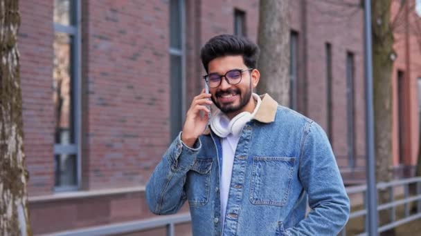 スタイリッシュな服で成功したインドのビジネスマン オフィスビルの近くに屋外で話して携帯電話を持っています 男は笑顔を捉え スマートフォン ビジネスライフスタイルのコンセプトを保持しています — ストック動画