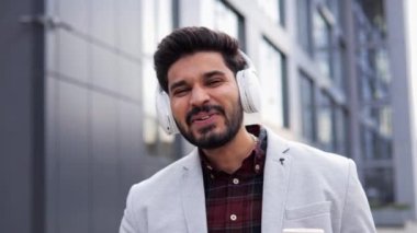 Sokakta tek başına dans ederken kulaklık takan mutlu yakışıklı Hintli adam. Bu gülümseyen genç melez adam, hipster, müzik dinliyor, açık havada kahve içiyor.