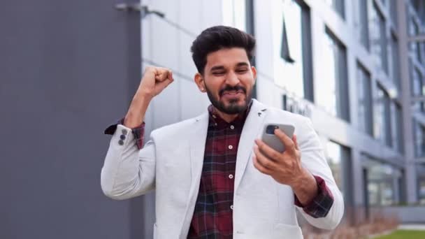 幸せな興奮インドの勝者ビジネスマンのリーダーの男は スマートフォンでビジネスチャットを持っている携帯電話の大きな勝利賞は 市内の屋外に立って衝撃的な顔を驚かせたとの良いニュースを受賞 — ストック動画
