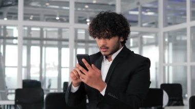 Başarılı ve yakışıklı İspanyol işadamı, engellenmiş bir banka kartı veya arızalı bir telefon yüzünden işlemleri tamamlayamadığı için ofisinde elinde bir cep telefonu tutuyor.