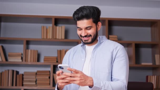 オフィス環境で幸せなインドのビジネスマンは 深く考えられているように見えるが 彼のモバイルデバイス上でタップしてスクロールします モバイル技術 生産性に関する概念 — ストック動画