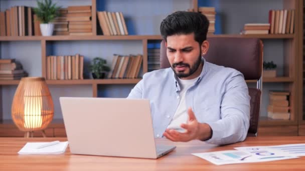 疲れ切った不安そうなインド人男性が財務報告書を事務所で完成させるのが難しい 男はノートパソコンを見て さまざまなチャートに囲まれ テーブルの上にグラフ 緊張とストレス — ストック動画