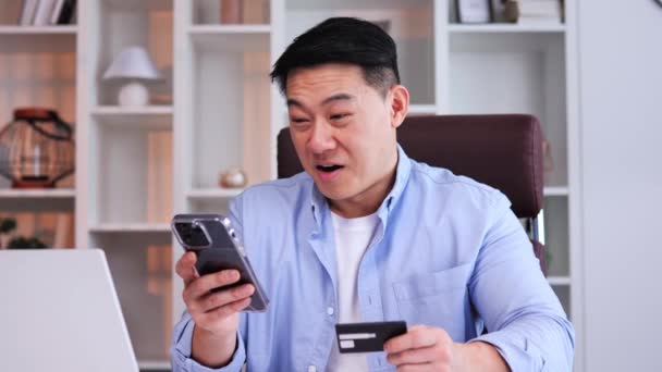 アジアのフリーランスは スマートフォンの銀行カードでオンライン決済を行うオフィスでクレジットカード電話を保持する成功を祝います スポーツへの賭けの側面は スマート投資の財務報酬を強調する — ストック動画