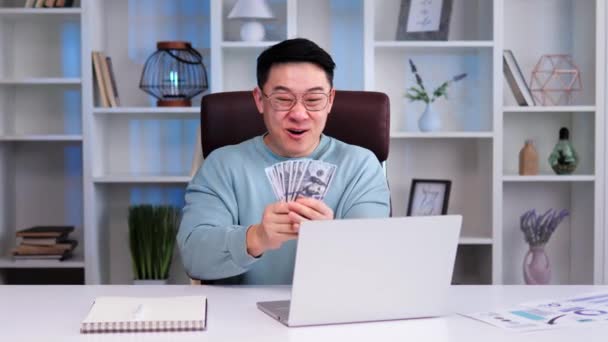 人们看到兴高采烈的韩国或中国商人手里拿着一大把钞票 在他直接凝视着笔记本电脑和钞票时 流露出兴高采烈 喜形于色的样子 很可能是在庆祝大获全胜 — 图库视频影像