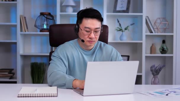 ビデオ会議電話を持つヘッドセットの韓国のビジネスマン 男性はオンラインビデオチャットで面接やコーチングセッションを実施しているようです 彼の自信とプロ意識を紹介します — ストック動画