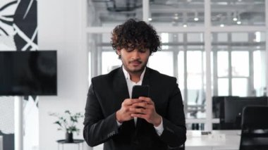 İspanyol bir Hintli işadamı, sosyal medyayla iletişim kurarken yüzünde mutlu bir gülümsemeyle, cep telefonuna bir mesaj yazarken ofis elbisesi içinde görülüyor. Adam cep telefonuyla çalışıyor.