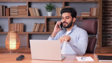 Latin kökenli işadamı ofis içi bilgisayarını kullanarak işine odaklandı. Adam bir telefona cevap vererek, uzak bir iş yerinde akıllı telefondan konuşarak birden fazla iş yapıyor. Gülümseyen adam ekran ekranına bakıyor.