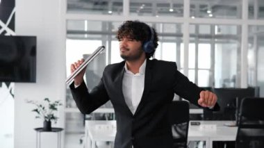 Komik, rahat Hintli mutlu iş adamı kulaklıklar takıyor ofis koridorunda dans eden Hintli adam eğleniyor özgür erkek iş başarısını kutluyor profesyonel başarı ya da zafer ödülü.