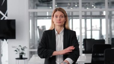 Kameraya kendinden emin bir şekilde el ele tutuşan şık bir iş kadınının portresi. Ciddi, odaklanmış, mavi gözlü bir kadın. Siyah kıyafetler giyiyor, modern ofis geçmişi var. İş adamları