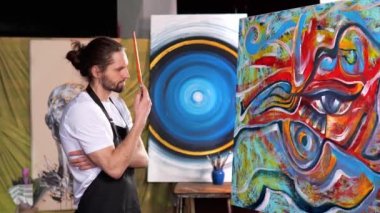 Beyaz tişörtlü yaratıcı sanatçı, resim yapmak için ilham ve motivasyon arayan saçlarını tararken dalgın görünüyor. Belki de yeni fikirler aramak ya da manzara değişikliği. 