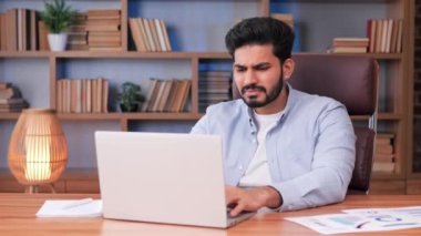 Kızgın Hintli adam ofiste oturuyor ve dizüstü bilgisayarla ilgili sorunları olduğunu düşünüyor. Sistem hatası, kötü e-posta, olumsuz haber, veri kaybı, yedek pil sorunları, parola hatası, kaydedilmemiş, kayıp bilgi onarımı gerekiyor