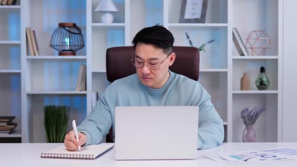 真剣にアジアの男性会計士は ノートパソコン上の電子銀行アプリを使用して 会計報告書を準備し お金を計算し 年間予算の概念を管理する計画 ペンの計算結果を保持オフィスに座って — ストック動画