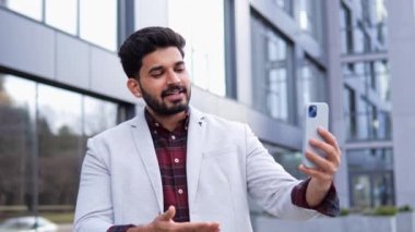 Takım elbiseli şık bir Hintli işadamı açık havada ortaklarla görüntülü konuşma yapıyor, teknolojiyle uzaktan iletişim kurmayı tartışıyor. Modern kurumsal iletişim ve liderlik
