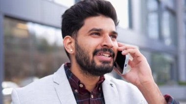 Açık havada telefon konuşması yapan yakışıklı Hintli adamın yakın plan portresi. Profesyonel iş adamı, sokakta yürürken telefonla konuşuyor. Adam ofisten uzak kaldığı için mutlu görünüyor.