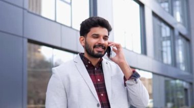 Şık, zarif, genç bir iş adamı telefon girişimcisiyle konuşuyor. Dışarıdaki cep telefonuyla iletişim kuruyor. Dışarıda telefonla konuşan yakışıklı Hintli adamın portresi.