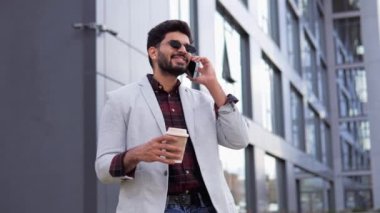 Hintli genç ve zeki iş adamı şehirde telefonla konuşuyor. Kahve fincanı tutan adam dışarıda arkadaşça sohbet ediyordu. İş konsepti için telekomünikasyon ve mobil ağ