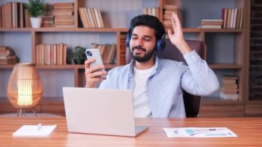 Ofiste dinlenen ve kulaklıkla müzik dinleyen sağlıklı, özgür Hintli adam stresin kutlu olsun. Çalışanlar işe ara veriyor. Başarılı Ciddi Adam İşyerinde Oturuyor ve Podcast dinliyor