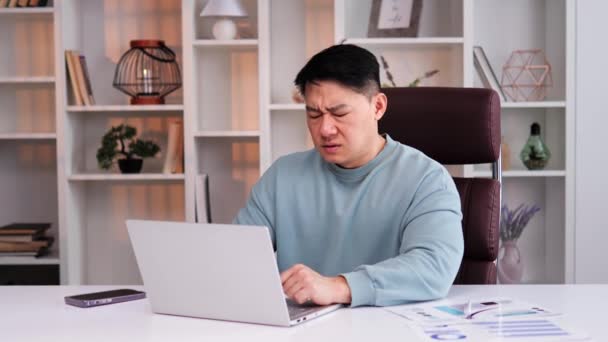 オフィスで病気のアジア人の男性は 痛みで額に手をつないで 重度の頭痛が発生します 仕事の過負荷とストレスを示す顔のクローズアップ 技術使用からの痛みと疲労の概念 — ストック動画