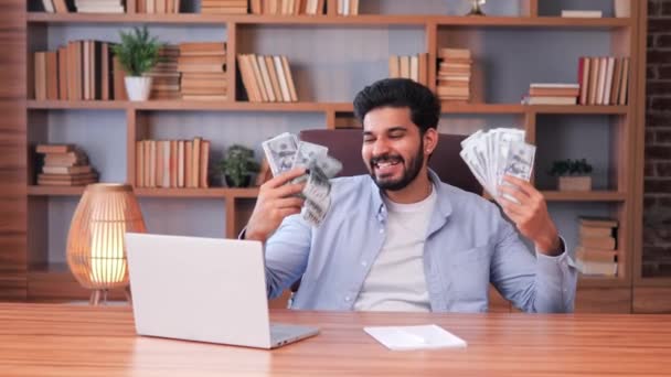 幸せな若いヒンドゥ教徒のビジネスマンは オフィスで働く中でお金の雨を楽しんでいます 億万長者のライフスタイルの概念 銀行券に囲まれ 喜びと満足の状態にあるようです — ストック動画