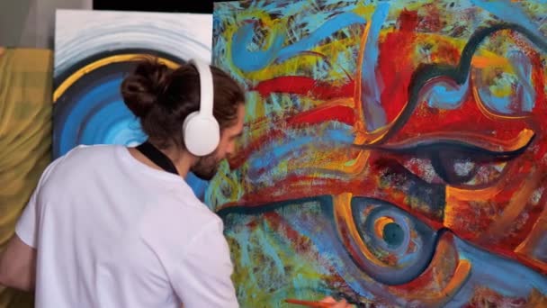 创意工作室 创新的熟练艺术家长发 耳机覆盖的绘画工艺杰作 画家用红色 黄色的颜料在一张大画布上创作了一幅令人惊叹的画 — 图库视频影像
