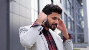 Mutlu Hintli Hintli serbest adam kulaklıklarını çıkarıyor. Güler yüzlü adam şehir sokağında dikiliyor kulaklıklarını çıkarıyor ve kameraya bakıyor. Cep telefonuyla müzik dinleyen adam.
