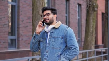 Başarılı Hintli işadamı şık kıyafetler içinde, dışarıda ofis binalarının yanında cep telefonuyla konuşuyor. Adam gülümseyerek ve elinde akıllı bir telefonla yakalandı. İş hayatı konsepti.