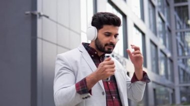 Bağımsız Hintli bir adam şehir caddesinde dururken kulaklıklarını gülümseyerek çıkarıyor. İnsan şehir gürültüsünden uzaklaşmak için cep telefonuyla müzik dinlemekten hoşlanır.