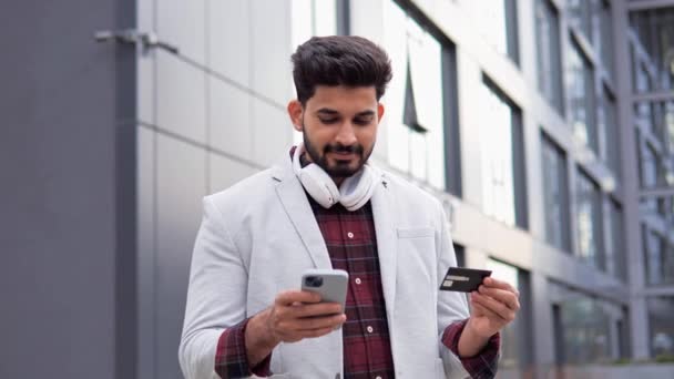 ハッピーインドの男性クライアントバイヤービジネスマン銀行の携帯電話アプリを使用してプラスチッククレジットカードを保持インターネットストアで商品を購入オンライン暗号通貨マネー取引屋外 — ストック動画