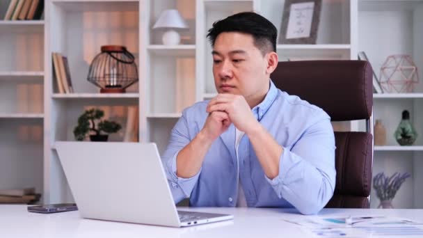 自信と集中したアジアのビジネスマンは 彼のラップトップコンピュータに熱心に取り組んで 現代のオフィスデスクに座っています 複雑な問題の解決策を考えているかのように — ストック動画