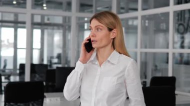 Ofisteki cep telefonuyla çalışan güzel ve odaklanmış genç bir kadın. Resmi giysiler giyen kadın, telefon görüşmesi sırasında profesyonel bir tavır takınırken akıllı telefon üzerinde çalışıyor.